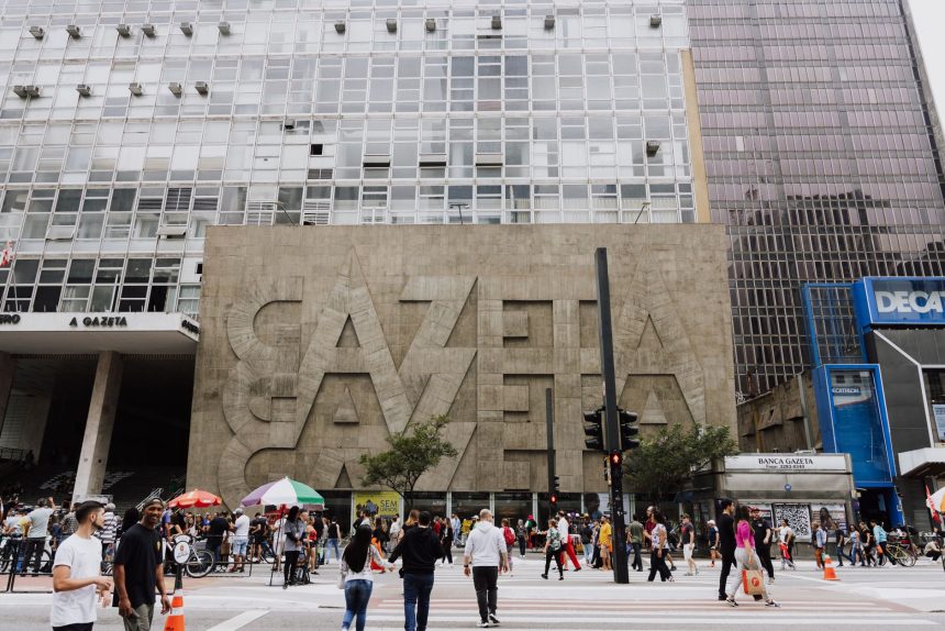 Pedestres caminham em uma rua movimentada diante do edifício Gazeta, na Avenida Paulista, em São Paulo.
