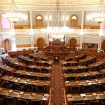 Vista ampla de um plenário legislativo ornamentado, com cadeiras vazias e lustres