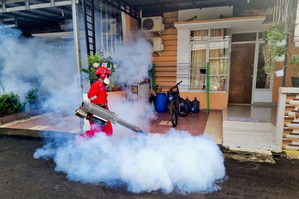 Profissional de controle de pragas utiliza uma máquina de fumaça para fumigar a área externa de uma casa.